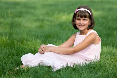 A pretty resting girl in pink is sitting on the summer grassの写真素材
