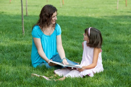 A daughter and her mother are talking about the book sitting on the meadowの写真素材