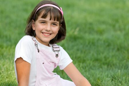 A portrait of a pretty smiling girl in pink sitting on the summer grassの写真素材