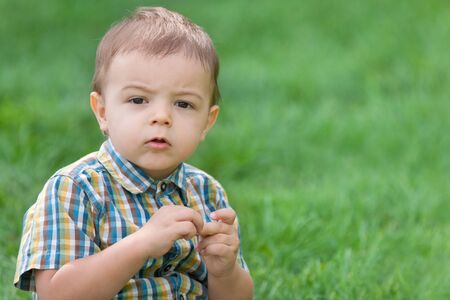 A  thoughtful boy in summer shirt is sitting on the green grassの写真素材