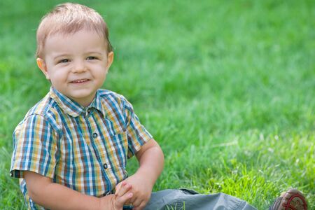 A handsome smiling boy is sitting outdoor on the green grassの写真素材
