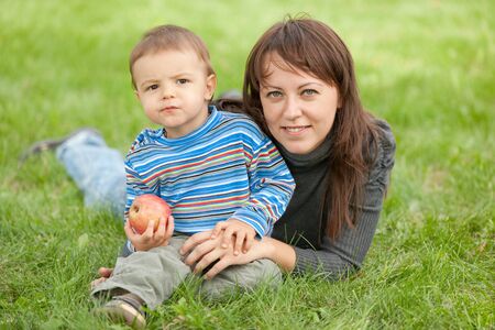 A mother and her son holding an apple are resting on the green meadowの写真素材