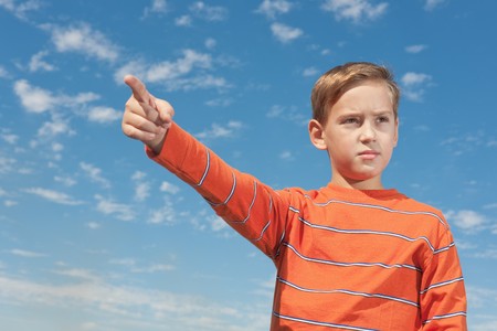 A serious boy is pointing right derection standing against the skyの写真素材
