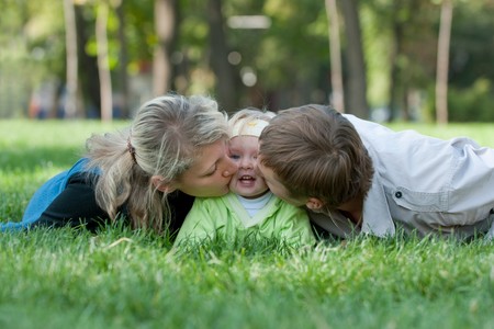 Father and mother are kissing their daughter from both sidesの写真素材