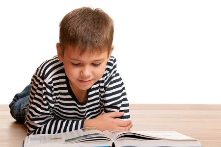 A lying kid is reading a thick book; isolated on the white backgroundの写真素材