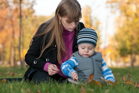 A mother is teaching her little son to draw while walking in the autumn parkの写真素材
