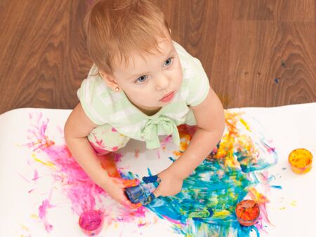 A toddler is painting a picture with her hands on the wooden floorの写真素材
