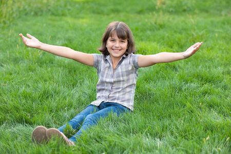 A cheerful laughing girl opens her hands sitting outside on the green lawnの写真素材