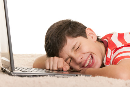 A handsome lying on the white carpet boy is crying with joy after computer game; isolated on the...