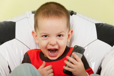 A little shouting boy is sitting on the football armchairの写真素材