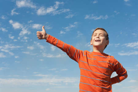 A happy kid is holding his thumb up and singing in front of the blue skyの写真素材
