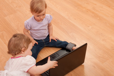 Two little girls are discovering a laptop on the floor