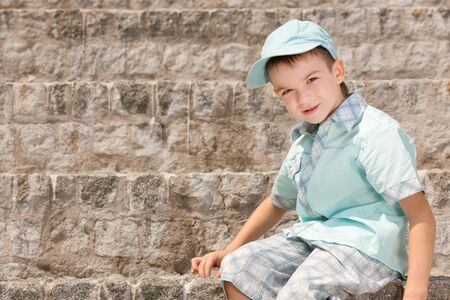 A smiling boy is sitting on the stone stepsの写真素材