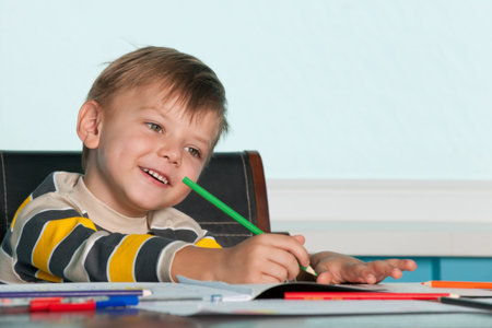 A smiling drawing little boy is sitting at the tableの写真素材