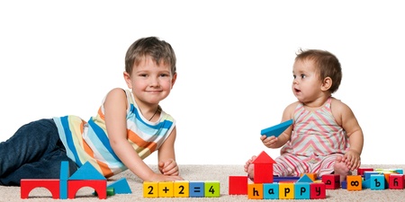 A smiling boy and a baby girl are playing with blocks on the carpet; isolated on the white backgroundの写真素材