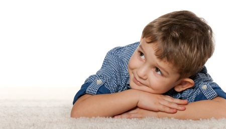 A thoughtful boy is dreaming on the carpet; isolated on the white backgroundの写真素材