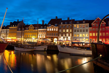 Copenhagen, Denmark - June 1, 2012: Boats at the harbor in Nyhavn at night against cafes with...
