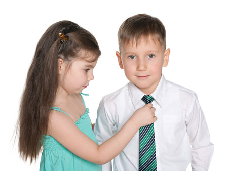A little girl helps a little boy in a white shirt with a tieの写真素材