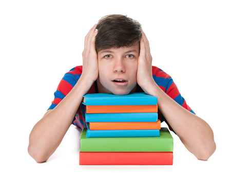 A portrait of a pensive teen boy on the floor near the pile of books on the white backgroundの写真素材