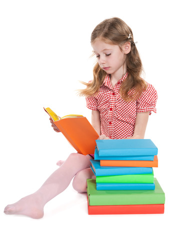 A young girl is sitting on the floor near the pile of books and readsの写真素材