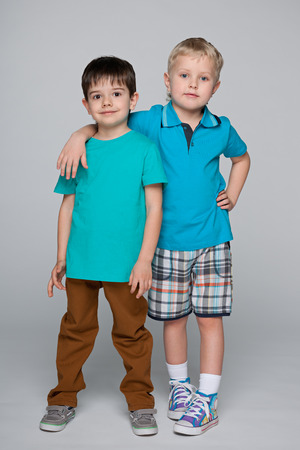 Two fashion smiling little boys are standing together against the gray backgroundの写真素材