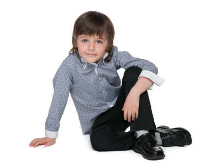 A smiling fashion preschool boy is sitting on the white backgroundの写真素材