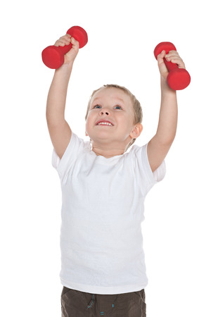 A preschool boy does morning exercises with dumbbells against the white backgroundの写真素材