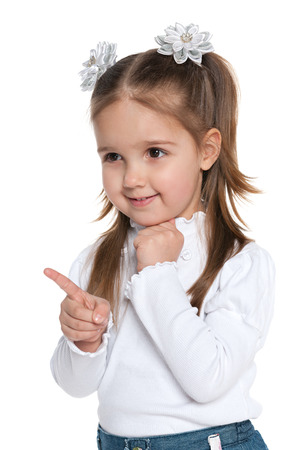 A smiling young girl shows her finger to the side on the white backgroundの写真素材