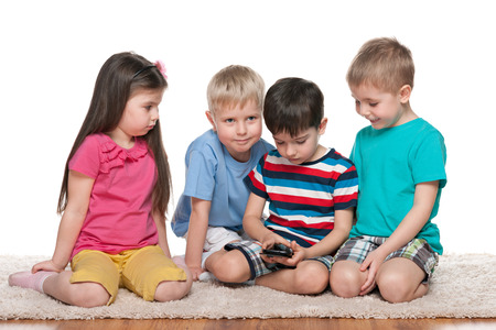 Four kids are playing with a new gadget on the white carpetの写真素材