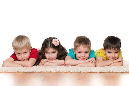 Four children are lying on the floor on the white carpetの写真素材