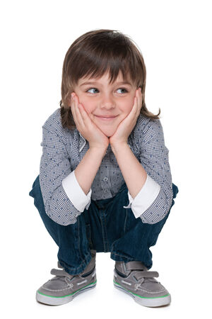 A smiling fashion little boy is sitting on the floor and looks asideの写真素材