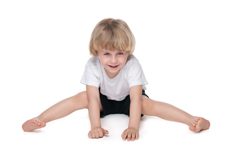 A smiling little boy performs gymnastic exercises on the white backgroundの写真素材