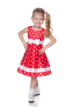 A smiling little girl in the polka dot dress is standing on the white backgroundの写真素材