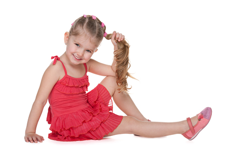 A cheerful little girl is sitting on the floor on the white backgroundの写真素材