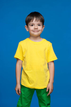 A cute little boy in the yellow shirt stands against the blue backgroundの写真素材