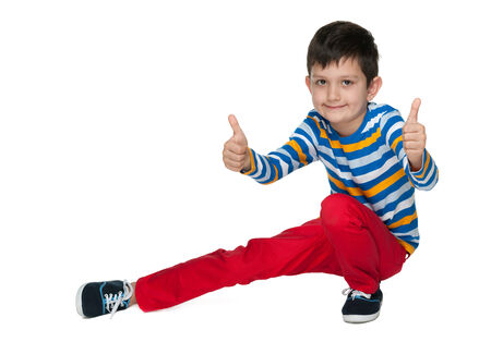A smiling little boy with his thumbs up is sitting on the white backgroundの写真素材