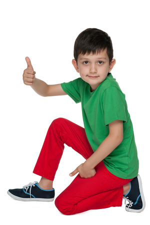A smiling little boy with his thumb up is sitting on the white backgroundの写真素材