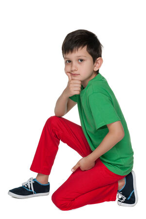 A pensive young boy in the green shirt is sitting on the white backgroundの写真素材