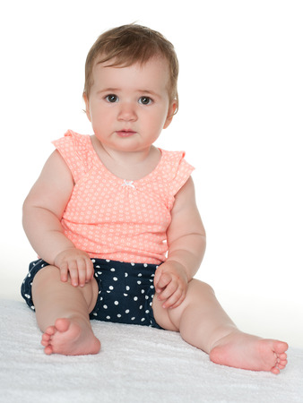 A cute thoughtful baby girl sits on the white towelの写真素材