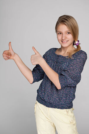 A pretty preteen girl holds his thumbs up on the gray backgroundの写真素材