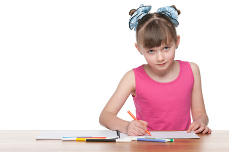 A clever schoolgirl sits at the school desk and drawsの写真素材