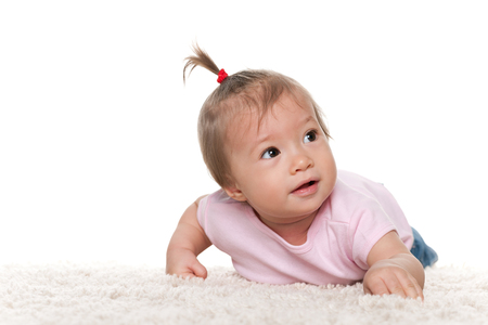 A cute infant girl is lying on the white carpetの写真素材