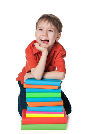 A happy little boy sits on the floor near the pile of books on the white backgroundの写真素材