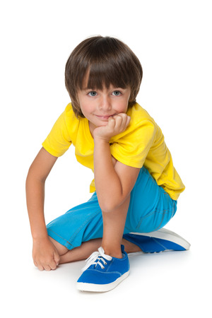 A smiling little boy in the yellow shirt is sitting on the white backgroundの写真素材