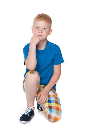 A pensive little boy in a blue shirt is sitting on the white backgroundの写真素材