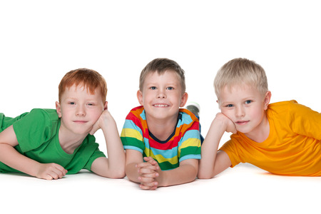 Group of three joyful boys are lying on the floor on the white backgroundの写真素材