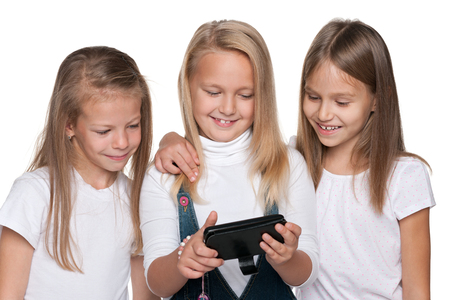 A group of three smiling girls with a smartphone on the white backgroundの写真素材