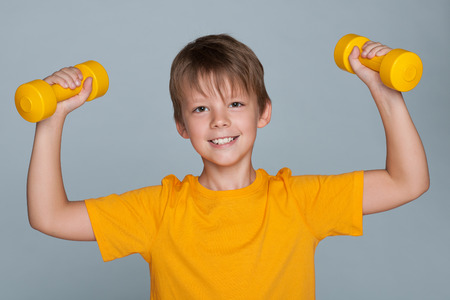 A cute boy do exercises with dumbbells on the gray backgroundの写真素材
