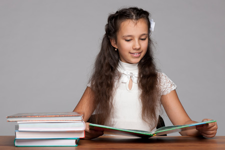 A smiling preteen girl is sitting at the desk and readingの写真素材