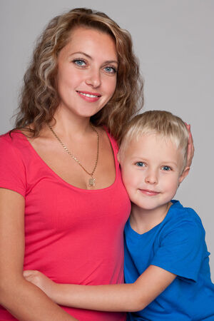 A smiling little blond boy hug his mother on the gray backgroundの写真素材